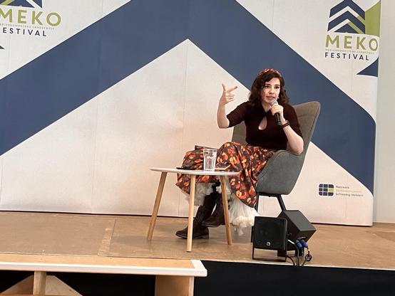 Marina Weisband auf einer Bühne, in einem Sessel sitzend mit Mikrofon in der Hand. Sie spricht gestikulierend und zählt gerade offenbar etwas auf.