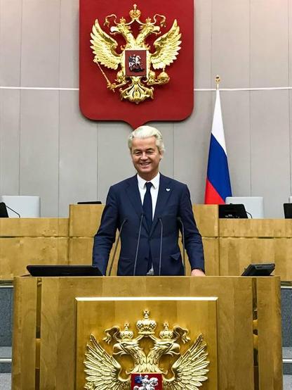 Foto van Wilders die vol trots in de Russische Doema op het sprekerspodium staat, zo'n 4 jaar na MH17, wanneer de schuldvraag van die aanslag al voor bijna 100% bij Rusland voor hun rekening staat. 
Een speld met de vlaggen van Rusland en Nederland prijkt op de kraag van zijn pak, als erkenning van zijn loyaliteit aan een vijandelijk en criminele  mogendheid.