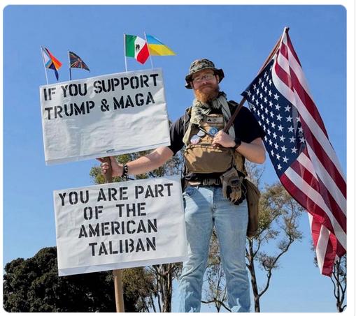 The screenshot shows a guy with a sign that reads:
"If you support Trump & MAGA, you are part of the American Taliban"