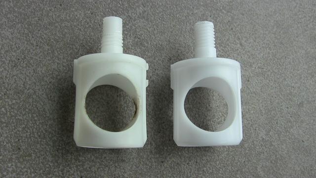 Zwei Bauteile mit Gewinde aus weißem Plastik. Liegend auf Fliesen.