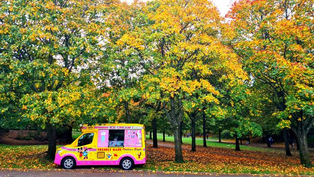 A brightly coloured ice cream van beneath trees covered in autumn leaves ib a Glasgow park.