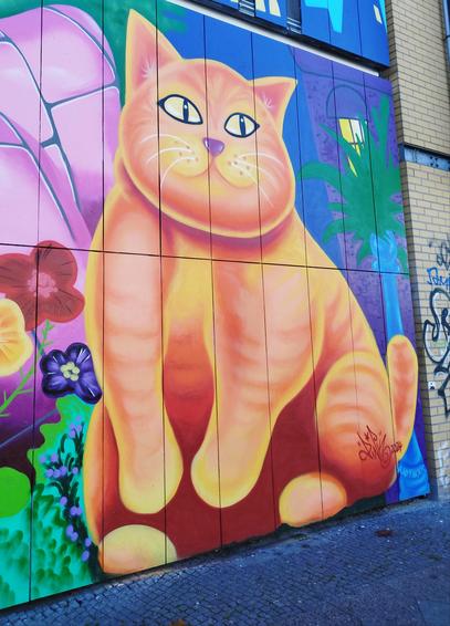 Streeart: an einer Hauswand : eine dicke orangefarbene sitzende Katze zwischen bunten Blumen