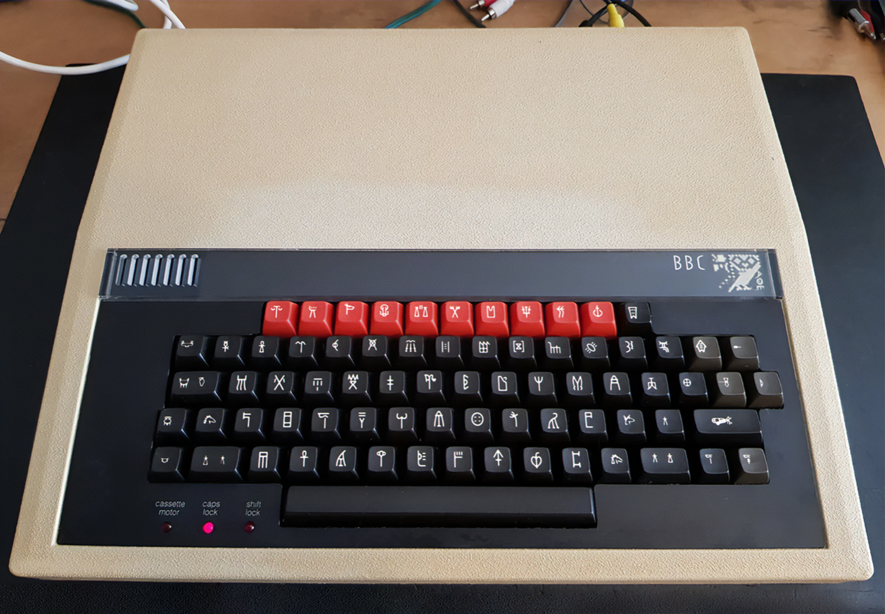 A photo of a BBC Microcomputer with beige body, black keyboard and red keys above. The legends on the keys are marked in Linear B
