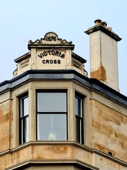 A pediment on the top of a corner tenement which says Victoria Cross 1876.