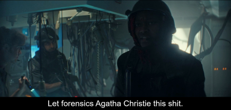 It’s a dimly lit room with bits of broken infrastructure, and surgical items dangling on straps. Diêm Camille walks towards the camera wearing a helmet and military gear. Two of her colleagues are visible in the background. The caption shows her say, ‘Let forensics Agatha Christie this shit.’