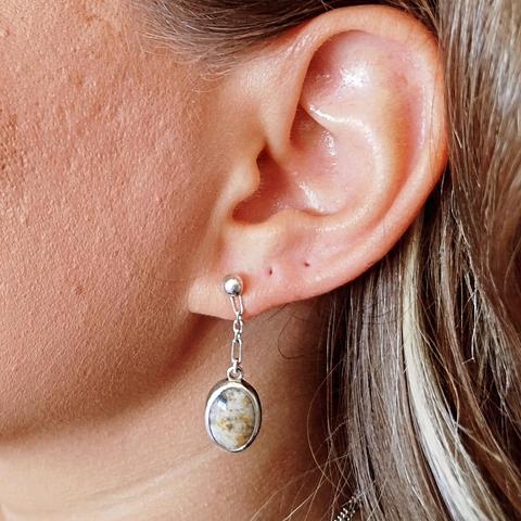 a silver earring with an oval gemstone. it's worn by a woman