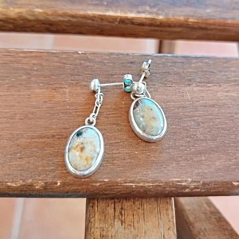 a pair of silver earrings with oval gemstones. it's on a piece of wood