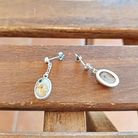 a pair of silver earrings with oval gemstones. the one earring it's upside down, you can see the back of it. the pair is placed on a piece of wood