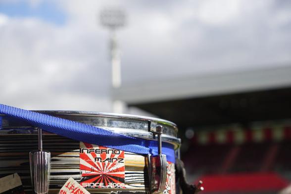 Im Vordergrund des Bildes im Anschnitt eine Trommel, darauf ein Sticker "Inferno Mainz since 2008", im Hintergrund in der Unschärfe ein Flutlichtmast. (Credit: Christoph Kessel)