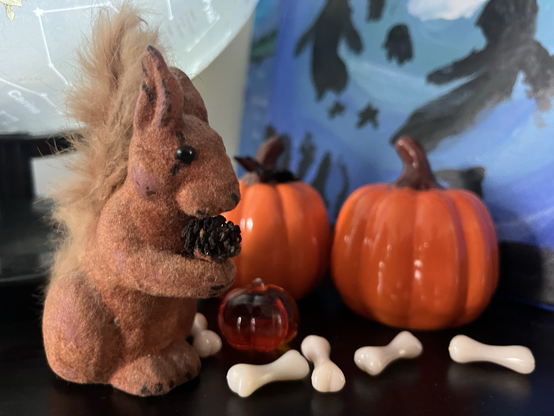 A small squirrel sculpture beside two ceramic pumpkins and some tiny plastic toy bones.