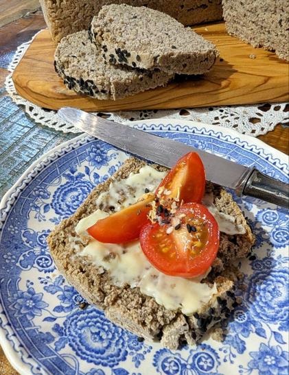 Weißer Porzellanteller mit blauem, floralem Muster auf Holztisch. Auf dem Teller eine Scheibe Kastenbrot mit Streichfett und Tomatenstücken. Ein Buttermesser liegt auf dem Teller. Dahinter ein Holzbrett mit einem kleinen, angeschnittenen Laib Kastenbrot und 2 geschnittenen Scheiben Brot.