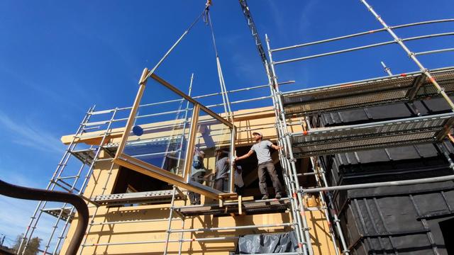 Une grue porte une fenêtre au bout d'une élingue devant la façade Duke maison en construction