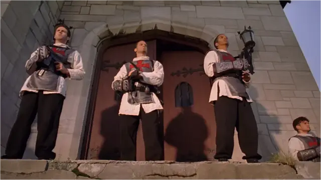 Screenshot from the film 'The Minion' (2016)

Upward-looking view of modern-day 4 Knights Templar standing in front of church doors looking outward on guard, machine pistols at the ready.