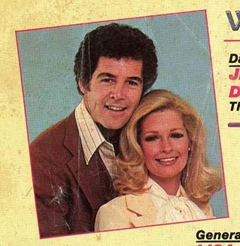 Vintage close-up of soap icons Deidre Hall and Jed Allan from the August 1980 cover of Rona Barrett’s Daytimers. Deidre wears a white blouse with a soft bow at the neck, her blonde waves styled in classic glamour. Jed sports a brown suit jacket over a striped shirt with a wide 70s collar, his dark curls framing a confident smile. Their expressions are warm and poised, evoking romance and star power. The image is framed by a colored border and partial magazine text, capturing the golden age of Days of Our Lives.