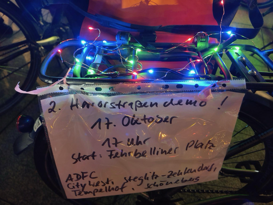 Auf einem Schild, das am Gepäckträger eines Fahrrads bei der Lichterfahrt des ADFC Berlin am 10.10.25 angebracht ist, steht, erhellt vom Licht einer Lichterkette: „2. Horrorstrassendemo 17. Oktober 17 Uhr Start: Fehrbelliner Platz ADFC CityWest Steglitz-Zehlendorf Tempelhof Schöneberg“