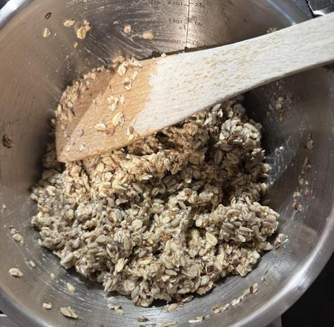 Die körnige Backmischung mit Wasser und einem Holzlöffel in einer Metallschüssel.