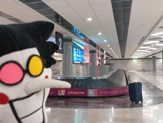 spamton sonriente frente a una banda transportadora y una maleta abandonada sin gente a la vista