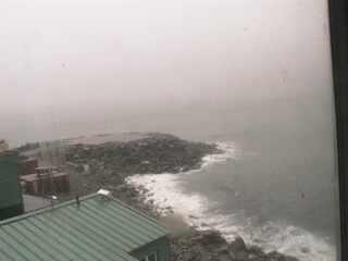 A low resolution image captured by a webcam overseeing a small peninsula with a few buildings at the front of the view.