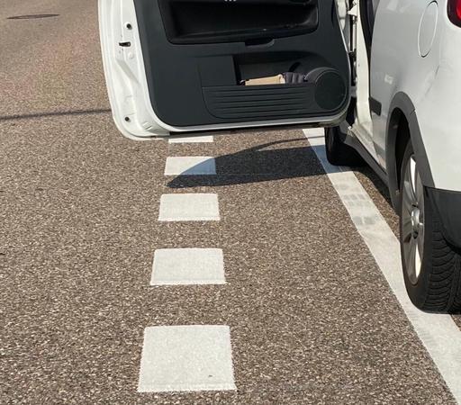 Bildausschnitt von einem Auto dessen linke Räder auf der Markierung eines Parkstreifens stehen.
Die geöffnete Tür geht deutlich über die markierte Dooringzone hinaus.