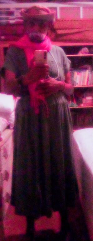 Photo of Ashwin Dixit, in a green dress, a cowboy hat, a pink scarf, and a pukka shell necklace.