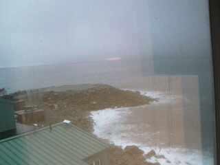 A low resolution image captured by a webcam overseeing a small peninsula with a few buildings at the front of the view.
