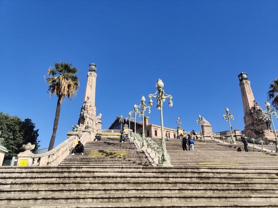Blick eine große Treppe hoch auf den Bahnhof Saint-Charles in Marseille. Es ist blauer Himmel.