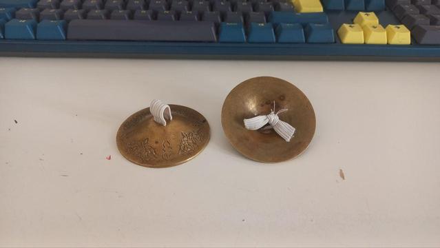 A couple of brass finger cymbals, one of the upside down, with new elastics.