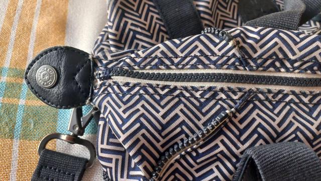 A handbag with a herringbone pattern in black, blue and white. The zipper is fixed with some crude stitching.
