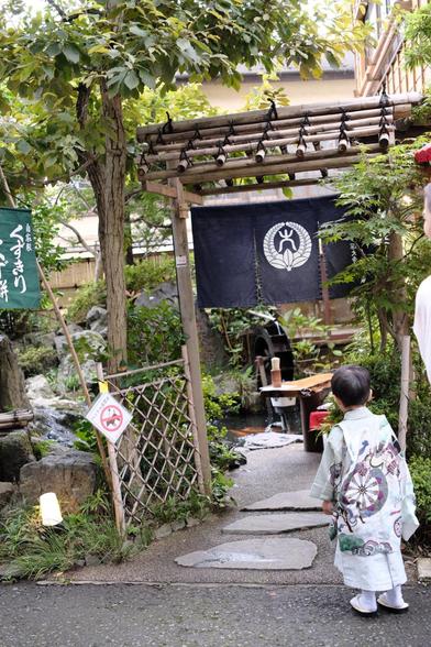 A little boy dressed in an elegant kimono in front of the entrance of a traditional 'café'