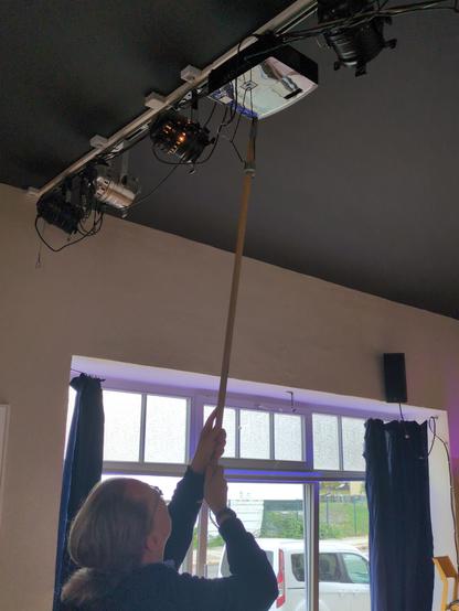 Bild zeigt Mensch, der Besentiel mit Panzertape geklebten Kleiderbügel zum einschalten des Beamers.