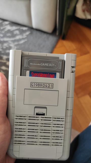 La même Game-Boy Lego vue de dos, les grilles des piles ont été reproduites dans le modèle, ainsi que le couvercle du compartiment à piles. On aperçoit la cartouche du jeu Super Mario Land insérée dans la console.