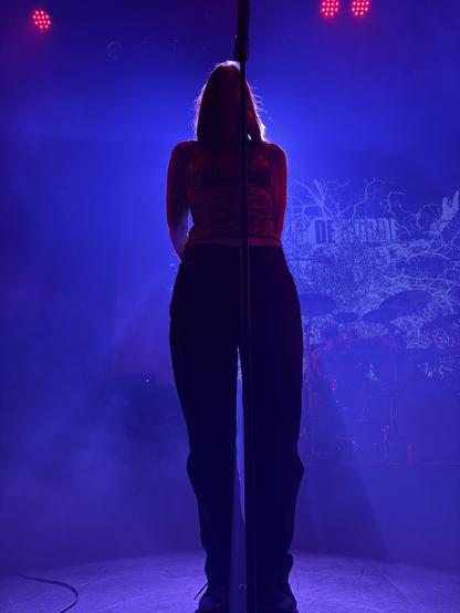 Charlotte Wessels providing guest vocals for Terzij De Horde at Soulcrusher. Standing behind the microphone arms on her back partially silhouetted by the stage light.