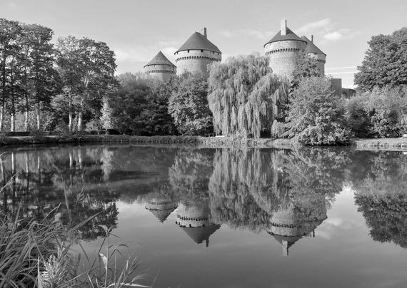 A castle with large towers surrounded by trees is reflected in the water.