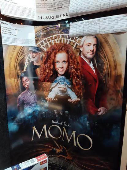 Kinoplakat von "Momo" durchs Ausstellungsfenster fotografiert zeigt eine rothaarige Momo mit Schildkröte Kassiopeia und weitere Figuren des Films.