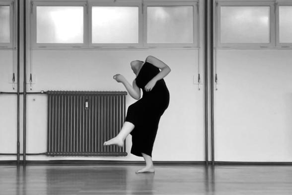 Black and white photograph of a dancer dressed in black (Clara Neumann) falling part sidewards part backwards while improvising in a studio, 2024