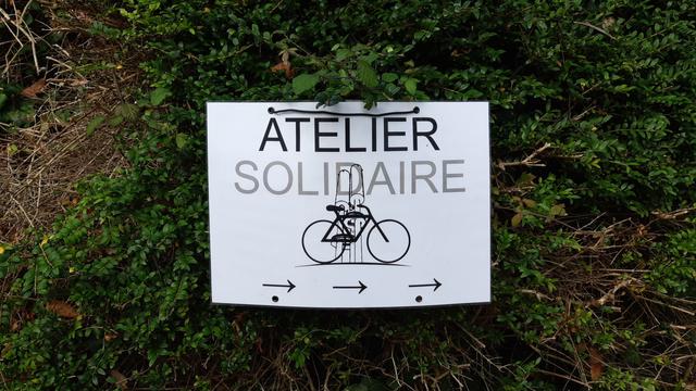 Panneau "Atelier Vélo Solidaire" sur un mur végétal