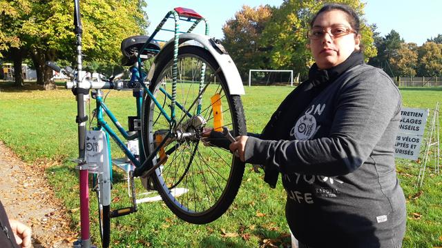 Jeune femme qui révise un vélo de ville à col de cygne sur un grand pré ensoleillé bordé d'arbres