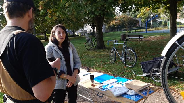 Femme et homme discutant un café en main, entre vélos et documentation, près d'arbres et d'un City-foot