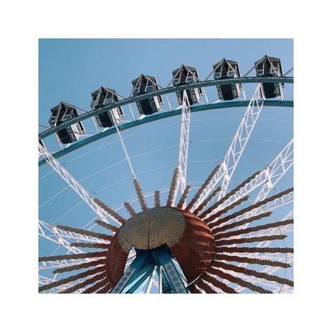detail shot of parts of a huge ferris wheel against the blue sky. the cabins actually look like tiny houses with gabled roofs. this image has a rather extreme bottom up perspective showing both parts of the center of the wheel as well as the outer ring