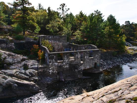 The concrete shell of an old mill beside a narrow and fast-moving river. The ruins are surrounded by a dense forest of conifers growing atop weathered granite. 

f9, 1/200s, iso200, 14mm (14-150mm)