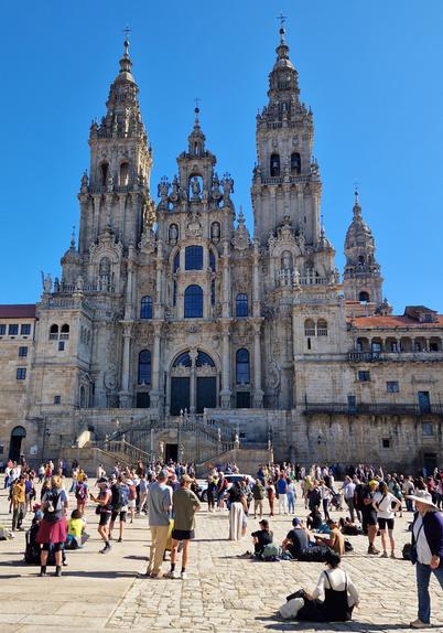 Katedralen i Santiago de Compostela med en klarblå himmel i bakgrunden. Mycket folk står och sitter på det stenlagda torget framför katedralen.