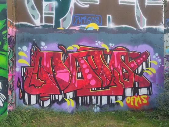 Graffiti piece on a concrete wall, grey background. The piece itself seems large red letters, flowing into each other, not sure what it spells. Pink accents like circles and paint drops in the red letters.  Some 3D effect because of white/black underside of the letters which is visible. In the bottom-right corner there are small letters spelling "OFMS", in yellow.