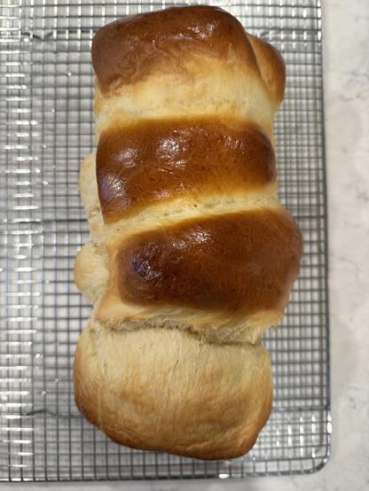 A loaf of golden-brown bread is cooling on a wire rack.