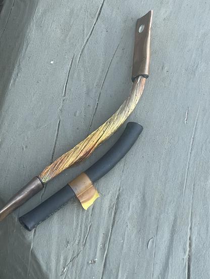 a 10" length of 1/0 copper stranded welding wire with copper lugs crimped on the ends.  the insulation has been cut off and lies next to it.  the bottom 2/3 of the stranded wire shows discoloration, as does a yellow strip of electrical tape around the insulation.