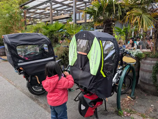 A Rad Power e-bike on the left, and my Tern HSD on the right, photo taken from the rear. My daughter is standing between the two bikes facing away.