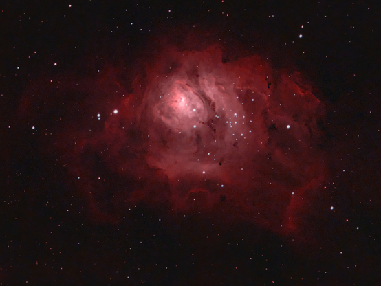 A red cloud of gas and dust suspended in the dark sky, illuminated by a plethora of stars. It reassembles the eye of a hurricane or a cave of soft intangible dust that swirls and sinks into a bright center.