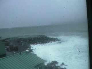 A low resolution image captured by a webcam overseeing a small peninsula with a few buildings at the front of the view.
