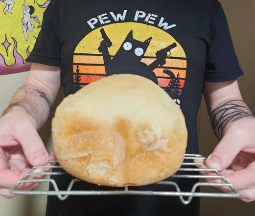 a photo of a small fresh loaf of bread on a cooking rack which is being held by me