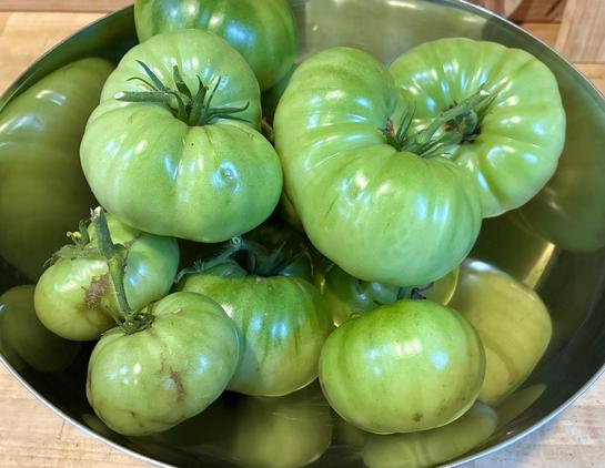 A bowl of green tomatoes on a wooden table.