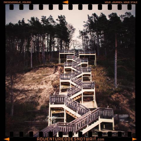 A winding wooden staircase through a forest in Międzyzdroje, Poland, symbolising the journey of adventure. The image captures earthy tones and natural textures, perfect for organic adventure apparel.